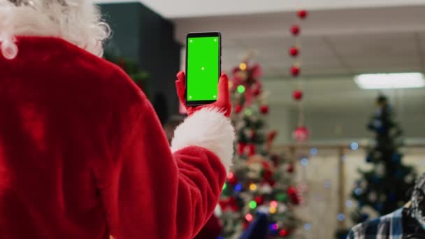 Valvoja joulu koristeellinen ostoskeskus yllään Santa Claus puku tilalla mockup puhelin, lukeminen myynninedistämistarkoituksessa joulutarjouksia asiakkaille vihreällä ruudulla talvilomakaudella, lähikuva - Materiaali, video