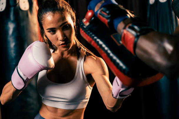 Aasian naaras Muay Thai nyrkkeilijä lyömällä kovaa nyrkkeily koulutus istunto, tuottaa lakko hänen sparraus kouluttaja yllään nyrkkeilyhanskat, esittelee Muay Thai nyrkkeily tekniikka ja taito. Virikkeitä - Valokuva, kuva