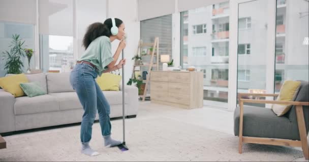 Music, headphones and woman dancing, cleaning and happy in home living room. Singing, broom hygiene and African person listening to audio, sound and moving to radio podcast in energy for house chores. - Materiał filmowy, wideo