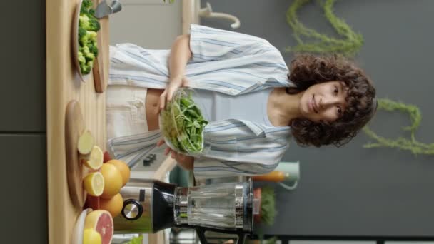 Pystysuora laukaus sovi tyttö bloggaaja seisoo keittiössä ja kertoo tuoreita vihanneksia kameran edessä, kun kuvaat terveellistä ruokaa resepti - Materiaali, video