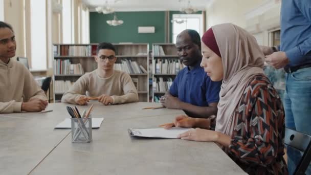 Группа студентов-этнических иммигрантов, сидящих за столом, получает тестовые документы по грамматике и начинает работать над ними - Кадры, видео