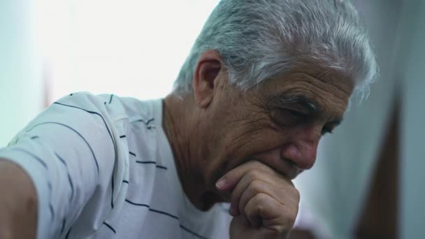 Przygnębiony siwowłosy starszy mężczyzna w głębokiej myśli, siedzący w ciemnym humorzastym pokoju - Materiał filmowy, wideo
