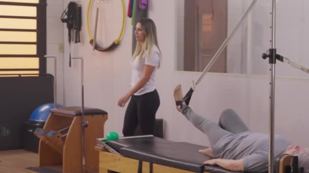 Trener Pilates pomaga seniorom w studiu fizjoterapeutów. Instruktor sportu pomaga starszemu mężczyźnie w ćwiczeniach, starość rutynowy styl życia - Materiał filmowy, wideo