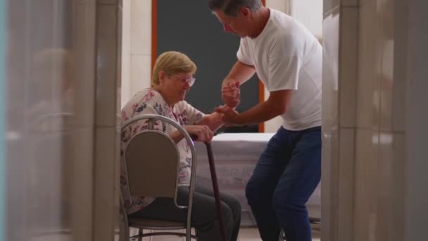 Echter Moment des erwachsenen Sohnes, der der älteren Mutter hilft, sich zu Hause vom Stuhl zu erheben - Filmmaterial, Video