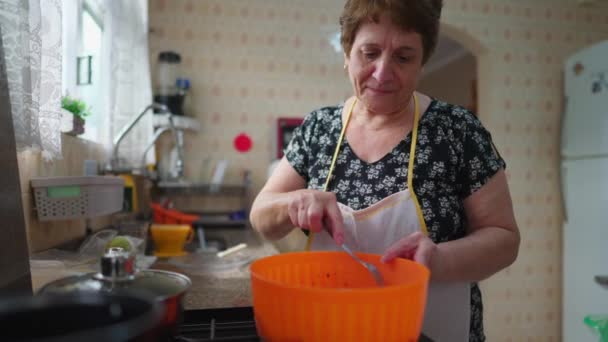 Сконцентрированная пожилая женщина готовит еду дома, бабушка в фартуке готовит обед - Кадры, видео