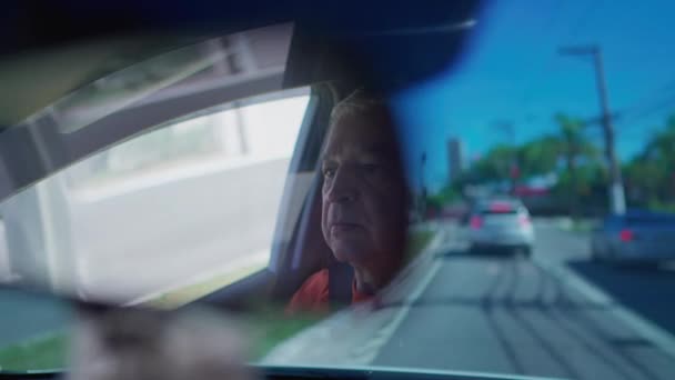 Senior man driving on city road seen through rear view mirror - Záběry, video