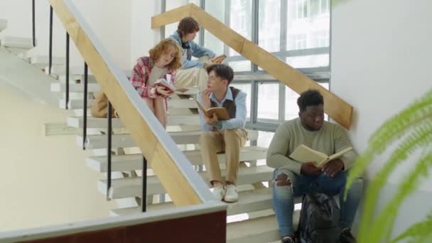 Etnik çeşitlilikte üniversite öğrencileri merdivenlerde oturmuş ders notlarını okuyor ve ödevlerini tartışıyorlar. - Video, Çekim