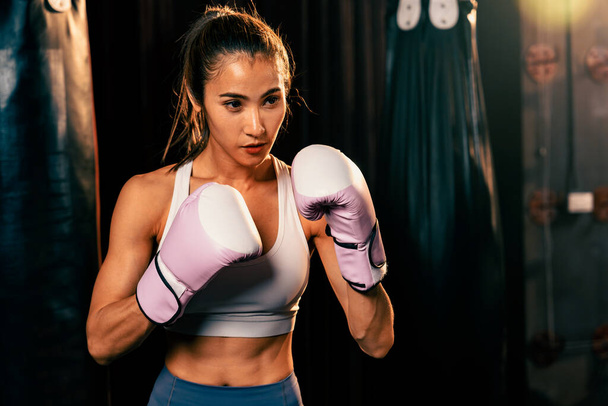 Kadın Muay Muay Tai boksörü savunma pozisyonu aldı. Spor salonunda eldiven giyiyordu. Poz vermeye, boks antrenmanına ve profesyonel dövüş sanatlarına hazırdı. Impetus - Fotoğraf, Görsel