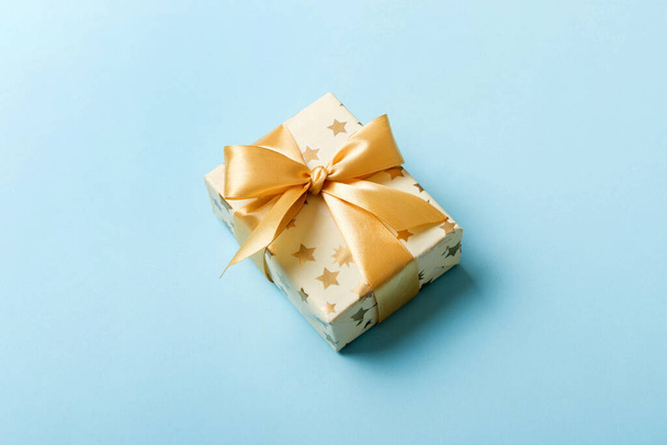 白い紙にクリスマスや他の休日の手作りプレゼントを包んだ色の背景に金リボンで。プレゼントボックス、カラーテーブルのギフトの装飾、コピースペース付きのトップビュー. - 写真・画像