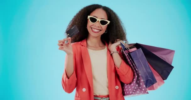 Portre, alışveriş çantası ve güneş gözlüklü kredi kartı olan bir kadın stüdyoda mavi bir arka plan modelleme alanında izole edilmiş. Moda satışları için plastik parası olan Afrikalı müşterinin mutlu, hediye ve yüzü. - Video, Çekim