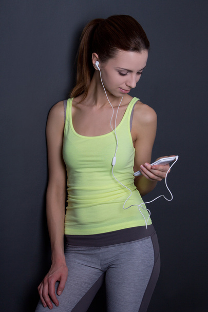 νεαρή γυναίκα σπορ ακούγοντας μουσική με τηλέφωνο πέρα από το γκρι - Φωτογραφία, εικόνα
