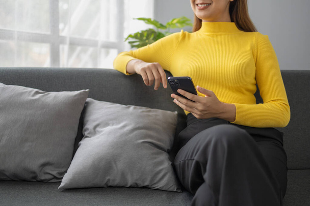 Азіатська жінка розслабляється на дивані в будинку, бізнес-леді проводить відпустку, дивлячись фільми, слухаючи музику і серфінг в соціальних мережах на смартфоні, спілкуючись і спілкуючись з друзями. концепція вихідних. - Фото, зображення