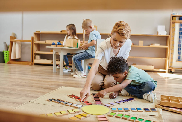 montessori anyag, afro-amerikai fiú játszik oktatási színes játék közelében boldog tanár, gyerekek - Fotó, kép
