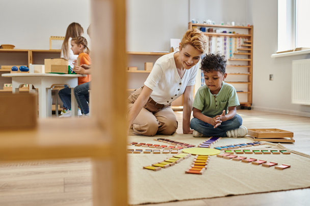 montessori materiaal, Afrikaanse Amerikaanse jongen spelen educatieve kleur spel in de buurt van vrolijke leraar, kinderen - Foto, afbeelding