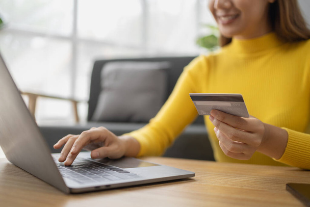 Азіатська жінка відпочиває у вітальні, бізнес-леді проводить свої святкові покупки онлайн на веб-сайті, вона купує на веб-сайті і платить кредитною карткою. Концепція використання кредитної картки для оплати онлайн. - Фото, зображення