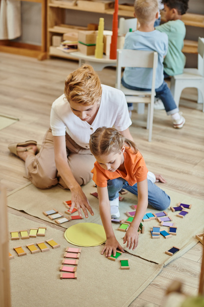 montessori materiał, dziewczyna gra kolor dopasowania gry w pobliżu radosnej nauczycielki, różnych chłopców - Zdjęcie, obraz