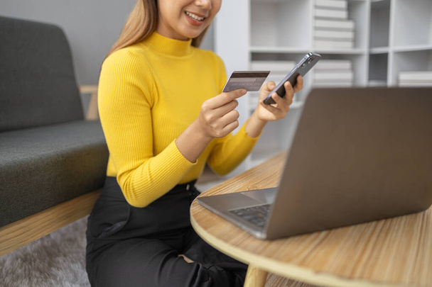 Азиатская женщина отдыхает в гостиной, деловая женщина проводит свой отпуск покупки в Интернете на сайте, она делает покупки на сайте и платить кредитной картой. Концепция использования кредитной карты для оплаты онлайн. - Фото, изображение