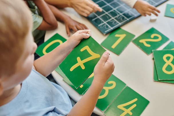 κορυφαία άποψη του αγοριού κρατώντας το νούμερο επτά κάρτα, μαθαίνοντας πώς να μετράνε στο σχολείο Montessori, μελέτη - Φωτογραφία, εικόνα