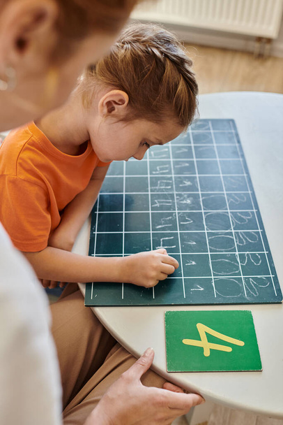Bayan öğretmen Montessori okulunda zeki bir kızı gözlemliyor, sayıyor, tahtaya yazı yazıyor, numaralar yazıyor. - Fotoğraf, Görsel