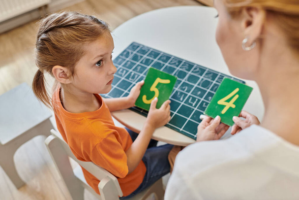 έξυπνο κορίτσι και δάσκαλος κρατώντας αριθμούς κοντά στο chalkboard, μάθηση μέσω του παιχνιδιού, καταμέτρηση, κορυφαία άποψη - Φωτογραφία, εικόνα