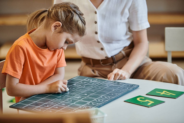 cute girl writing on chalkboard near numbers, learning through play, insegnante, concetto Montessori - Foto, immagini