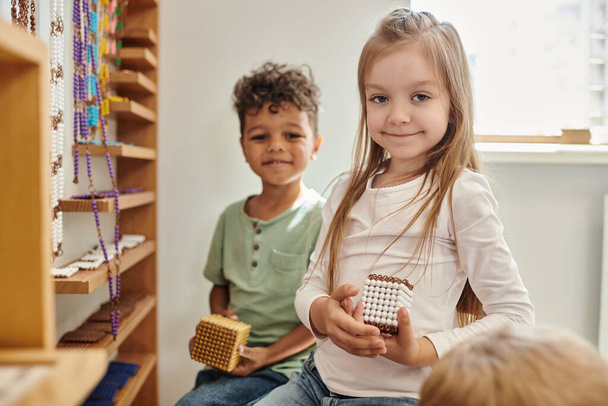 cheerful girl holding cube with beads near african american boy, diversity, Montessori school - Valokuva, kuva