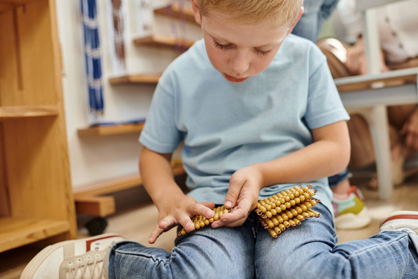 Sarışın çocuk, Montessori boncuklarını tutuyor, sayıyor, oyun oynayarak öğreniyor, erken eğitim alıyor. - Fotoğraf, Görsel