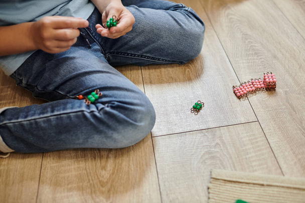 cropped view of boy sitting in jeans on floor, playing with Montessori beads material, game - Photo, Image