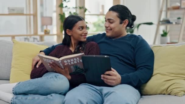Couple, tablet and reading a book on a home sofa for search, internet and knowledge or relax. Happy man and woman together on couch with technology and novel for entertainment, learning or connection. - Footage, Video