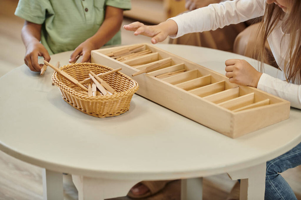 καλλιεργημένη άποψη πολυεθνικών παιδιών που παίζουν με ξύλινα μπαστούνια κατά τη διάρκεια του μαθήματος στο σχολείο Montessori - Φωτογραφία, εικόνα