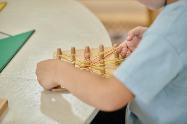 bijgesneden mening van jongen spelen met elastiekjes en houten stokken op tafel in Montessori school - Foto, afbeelding