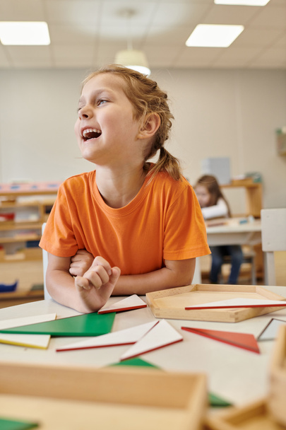 niño feliz mirando lejos cerca de materiales didácticos de madera en la clase de la escuela montessori - Foto, Imagen