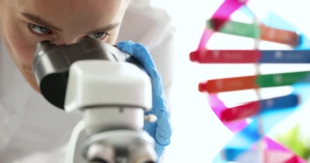 Nainen tiedemies etsii mikroskoopilla lähellä keinotekoinen malli DNA molekyyli 4k elokuva hidastettuna. Geenitutkimuksen geenitieteen käsite - Materiaali, video