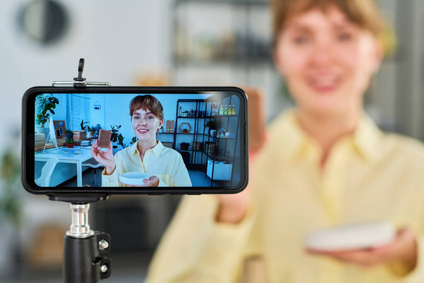 Focus op smartphone scherm met vrolijke jonge vrouw met handgemaakte zeep bar en reclame voor nieuwe self care items om haar abonnees - Foto, afbeelding