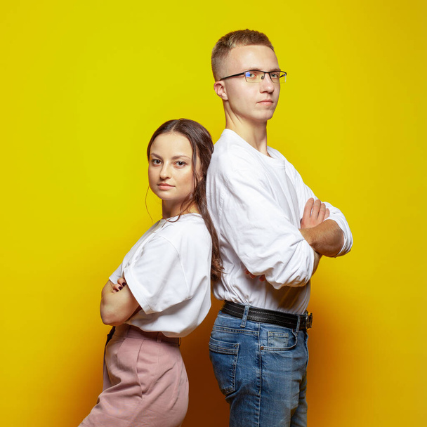Starker ernsthafter selbstbewusster junger Mann und Frau Rücken an Rücken mit verschränkten Armen auf gelbem Hintergrund - Foto, Bild