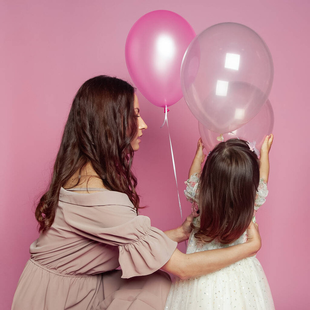 Morena mãe e filha com balão no fundo do estúdio rosa. Mãe e bonito criança bebê menina - Foto, Imagem