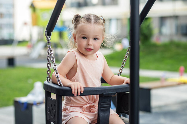 Kid toddler girl swinging on playground swing. Kid playing on school or kindergarten yard. Summer time. - Photo, Image