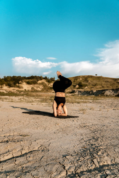 Egy nő jógázik és szöget verve áll a sivatagban napnyugtakor. A jóga fogalma és a körmökön állás - Fotó, kép