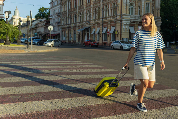 Mosolygó fiatal nő bőrönddel a városban - Fotó, kép