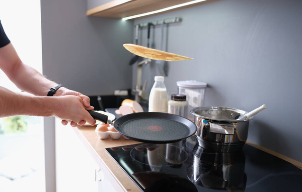 Hands hold black iron pan and toss pancake into air. Cooking pancakes at home in kitchen - Foto, Imagem