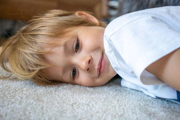 自宅のカーペットの上に横たわっている笑顔の小さな男の子の肖像画を閉じる - 写真・画像