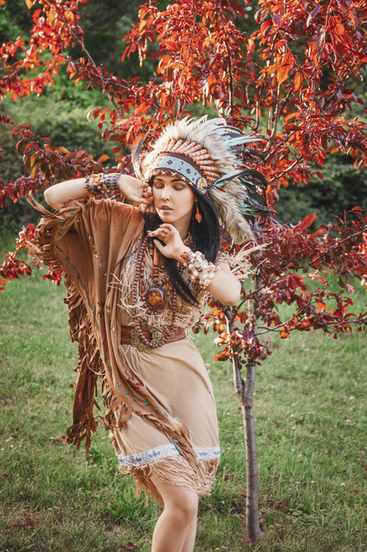 Intiaaninaisen muotokuva ulkona. Kaunis etninen nainen, jolla on torakka päässään. Nainen boheissa vaatteissa seisoo puun alla. - Valokuva, kuva