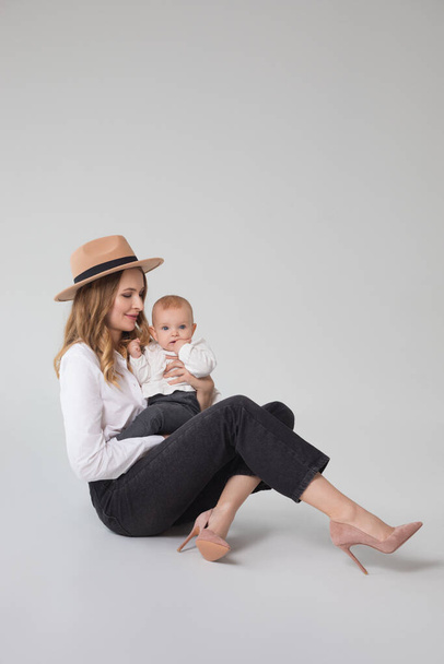 mode portret van moeder en kind zitten op de vloer in de studio, jonge vrouw met haar dochter - Foto, afbeelding