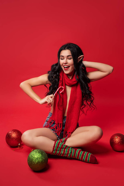 jovem mulher sexy em traje de elfo e com orelhas de elfo no fundo do estúdio vermelho, estilo pin-up, venda de ano novo - Foto, Imagem