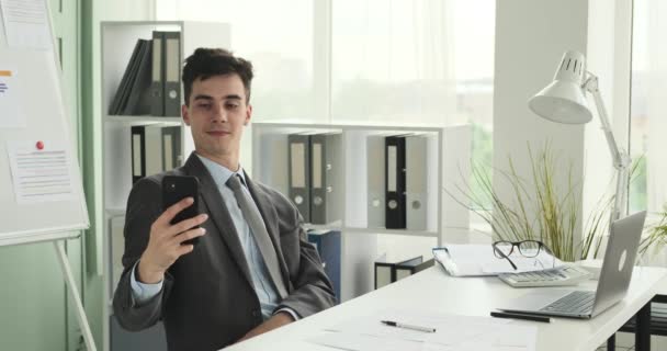 Office worker is seen taking a selfie for social media. With a smartphone in hand and a playful expression, he captures a moment of enjoyment and shares it with his online community. - Footage, Video