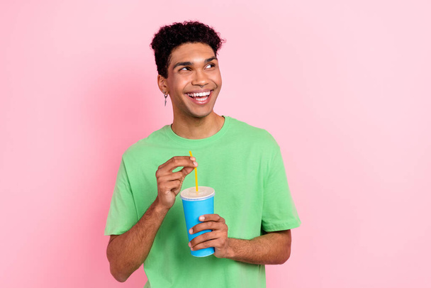 Fotografie přemýšlivý funky muž oblečený zelený tričko pití limonády hledá prázdný prostor izolované růžové barvy pozadí. - Fotografie, Obrázek