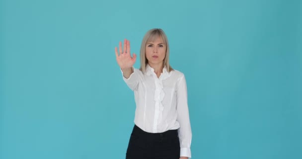 Distressed woman is shown making a stop gesture with her hand on a serene blue background. Her troubled expression and the raised palm indicate her desire to halt or prevent something. - Footage, Video