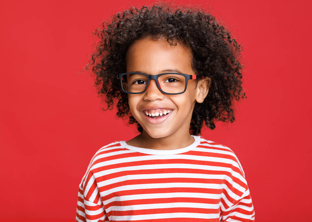 Entzückte afroamerikanische Schülerin lacht vor rotem Hintergrund in die Kamera, während sie in der Schule Spaß hat - Foto, Bild