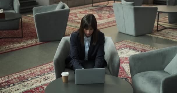 Ελκυστική και εκλεπτυσμένη επιχειρηματίας, όπως αυτή χαριτωμένα δακτυλογραφεί στο laptop της, ενώ κάθεται σε μια άνετη καρέκλα. Η συγκροτημένη και σίγουρη συμπεριφορά της συμπληρώνει τις ικανότητες δακτυλογράφησης.. - Πλάνα, βίντεο