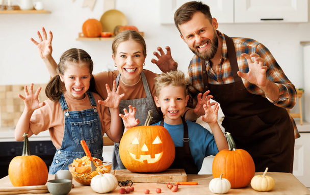 Onnellinen perheen äiti, isä ja lapset hymyilevät kameralle ja pelottava ele, kun taas tehdä jack-o-lyhty kurpitsa juhlan aikana, saada valmis halloween - Valokuva, kuva